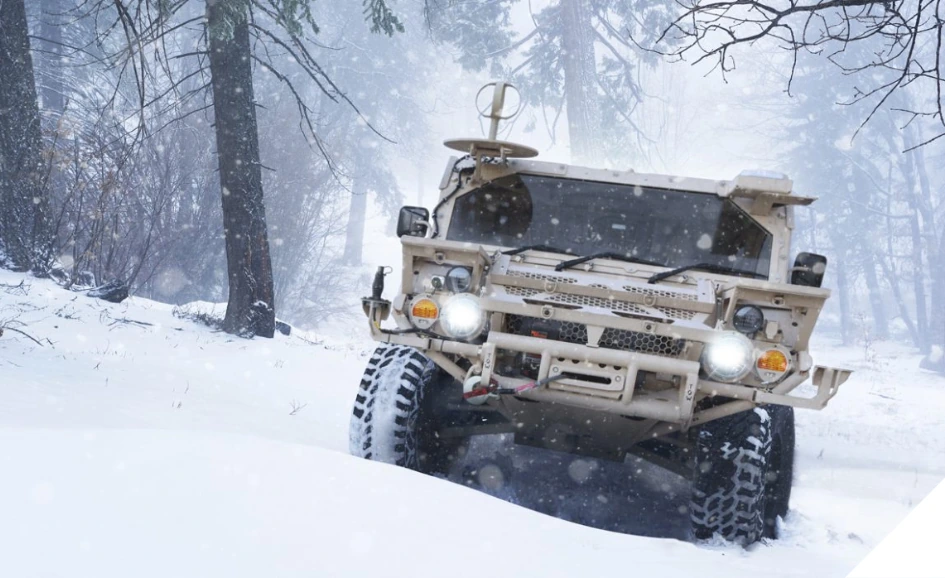 Flyer 72-HD tactical vehicle driving through snow-covered forest terrain.